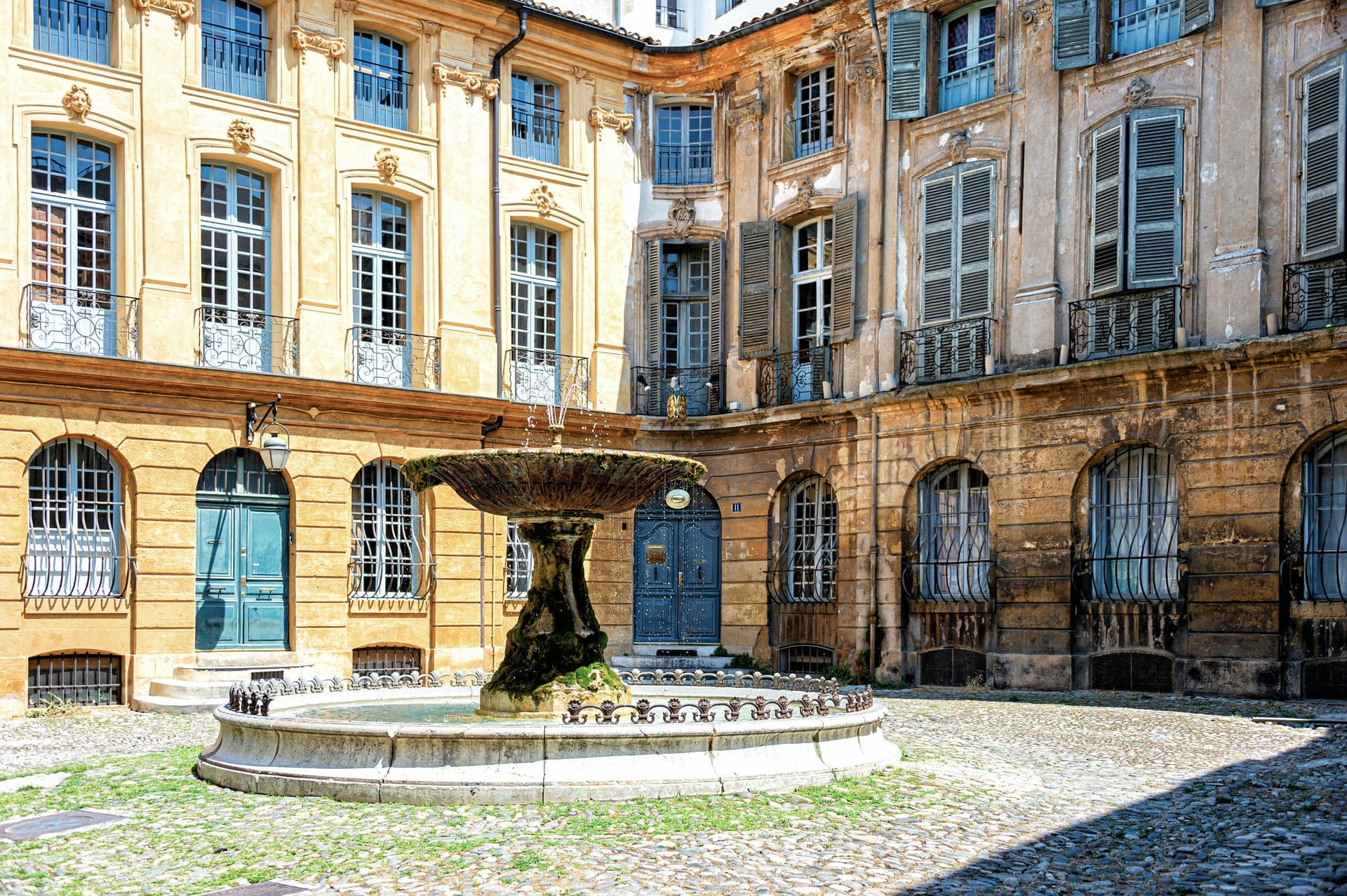 Une fontaine et des façades provençales aux volets bleus à Aix-en-Provence.