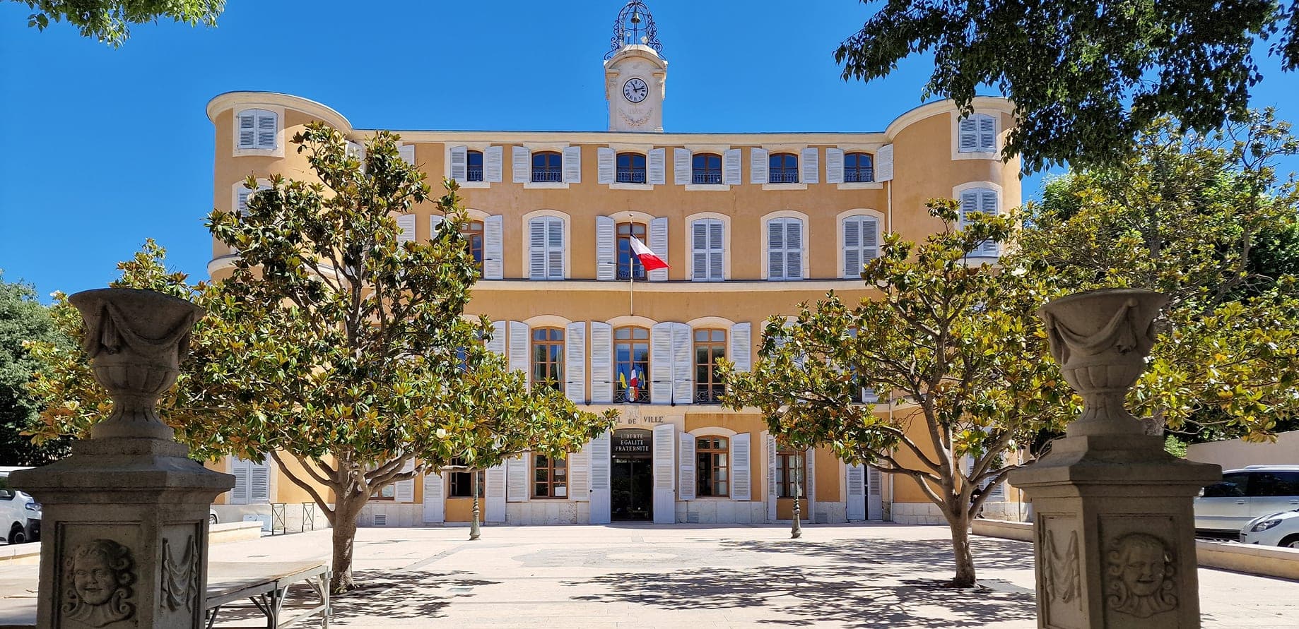 La façade de l’hôtel de ville de Gémenos, son horloge et les arbres de la place.