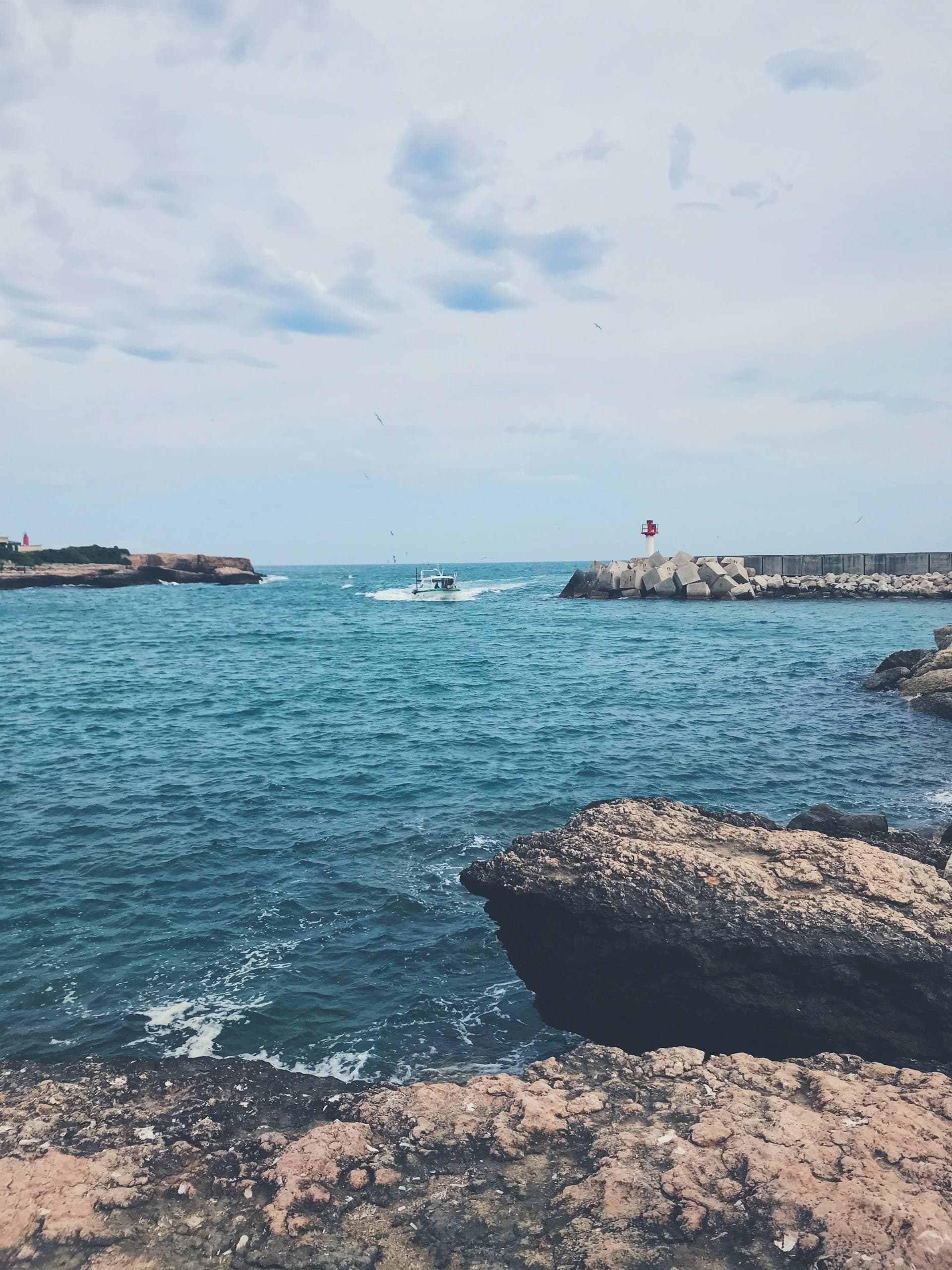 Une entrée de port du littoral de Martigues, avec sa digue, son phare et les rochers au premier plan.